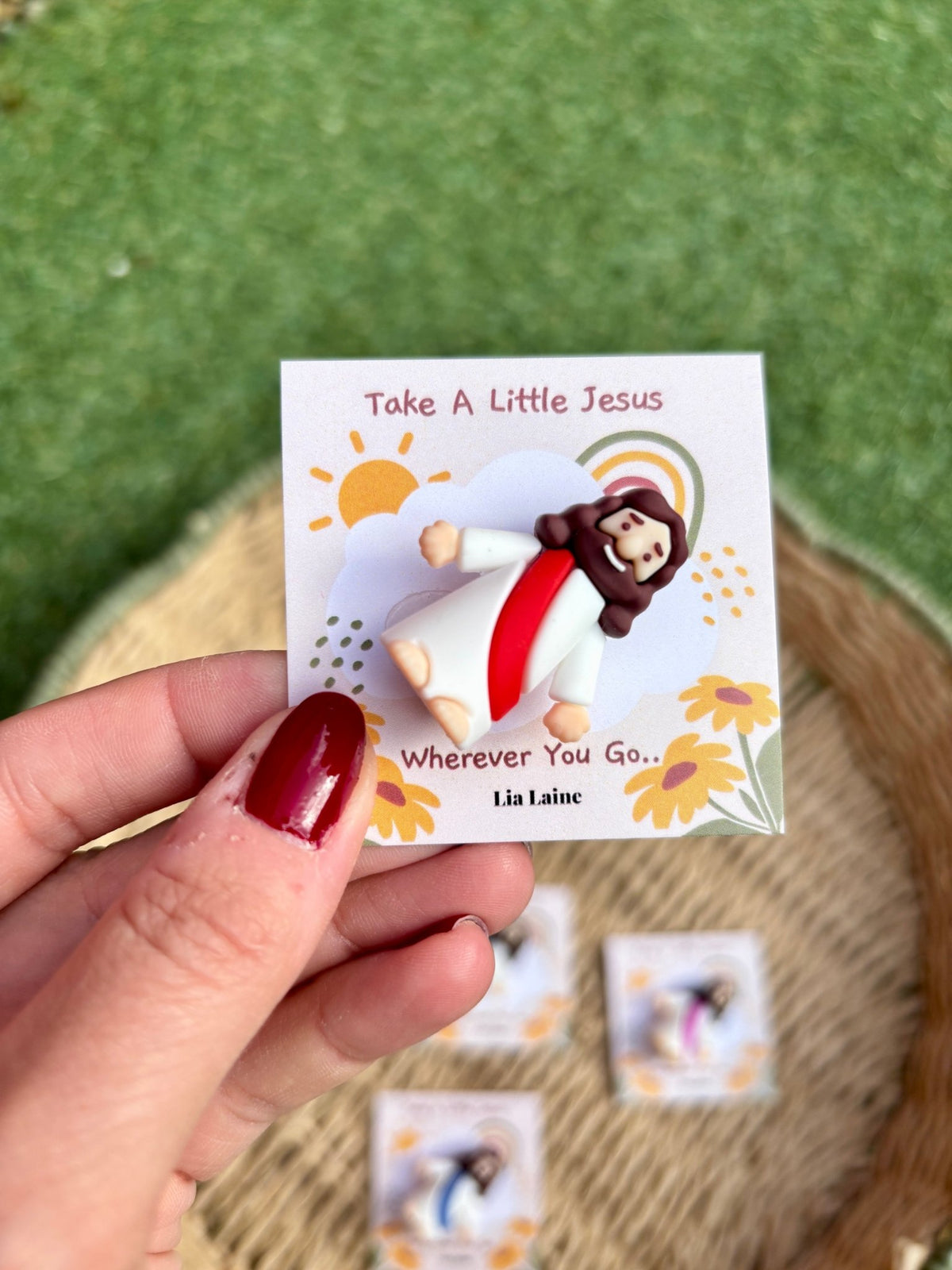 Jesus Pocket Card, red mini Jesus figurine on a sun and rainbow backing card with other colours and grass in the background.