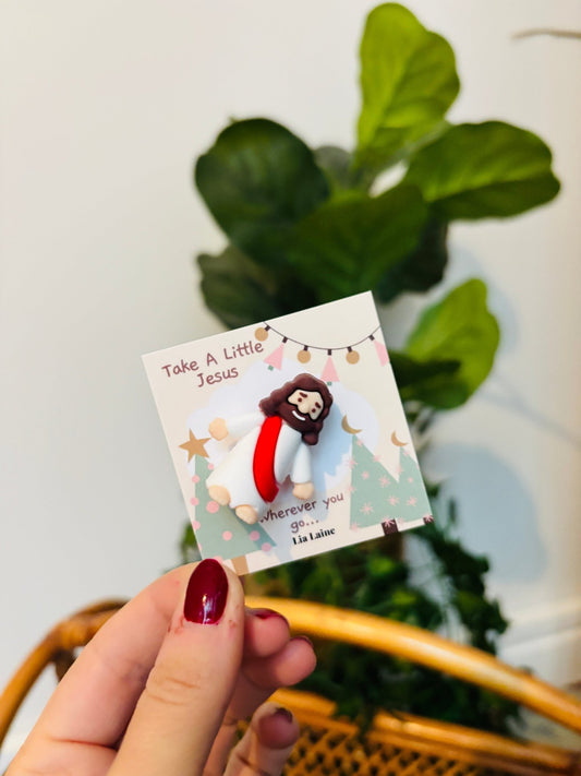 A mini Jeuss figurine on a Christmas design backing card with a plant and wicker basket in background