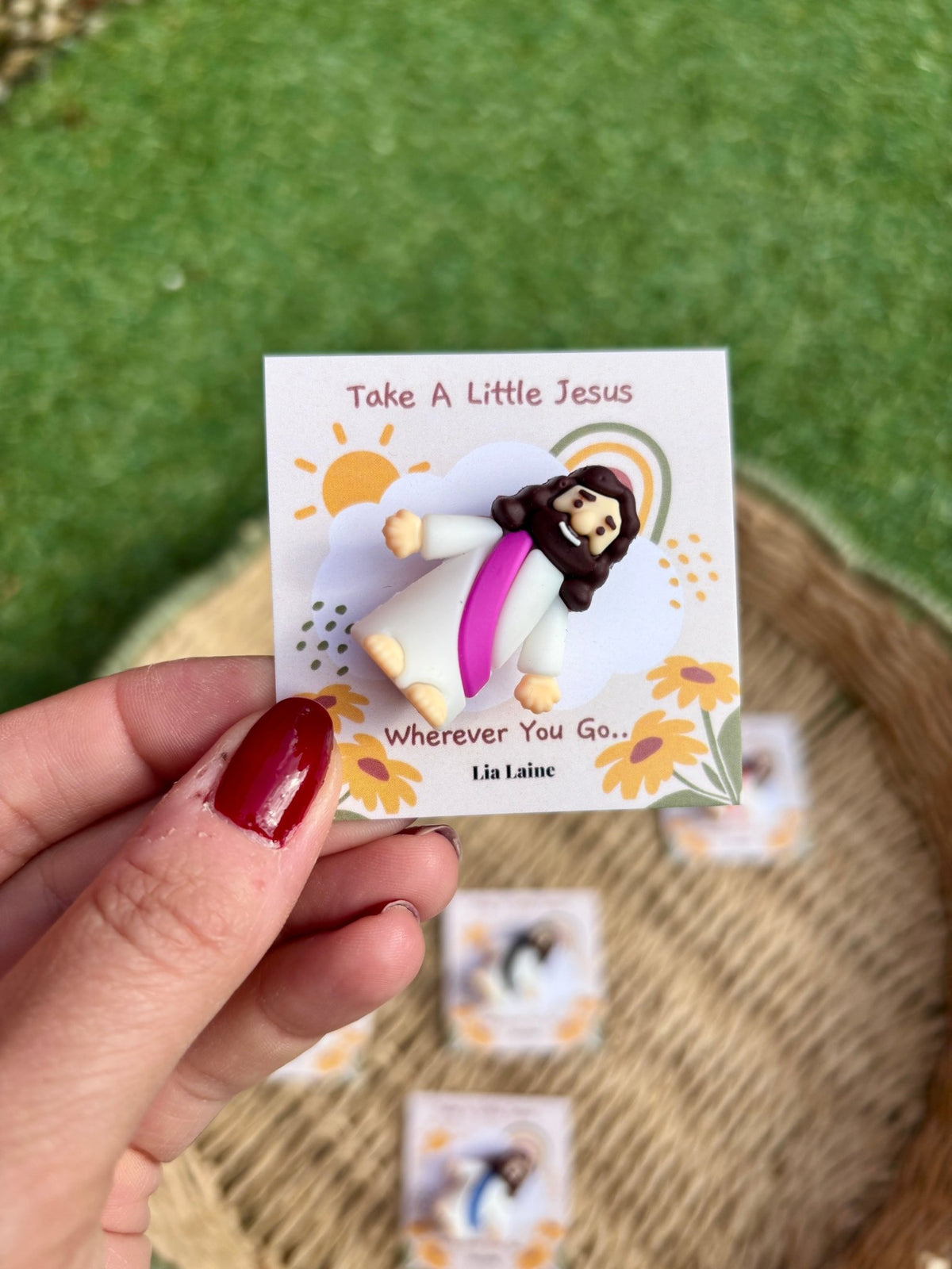 Jesus Pocket Card, purple mini Jesus figurine on a sun and rainbow backing card with other colours and grass in the background.
