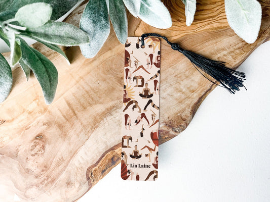 Yoga poses bookmark - a metal bookmark with tassel of a collection of yoga poses on a wooden table and greenery background
