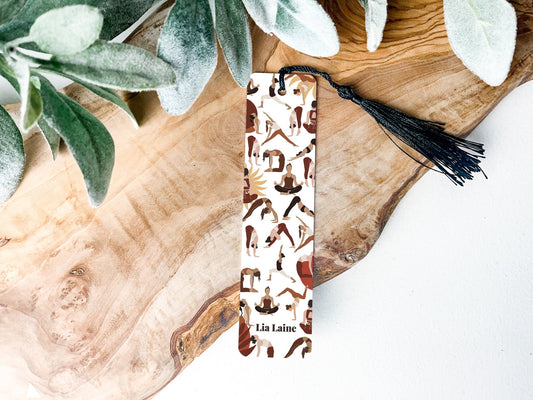 Yoga poses bookmark - a metal bookmark with tassel of a collection of yoga poses on a wooden table and greenery background